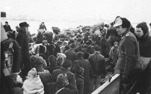 Ein Schwarzweißfoto zeigt ein mit Menschen gefülltes Boot in Pillau im Jahr 1945. Die Menschen tragen Wintersachen.
