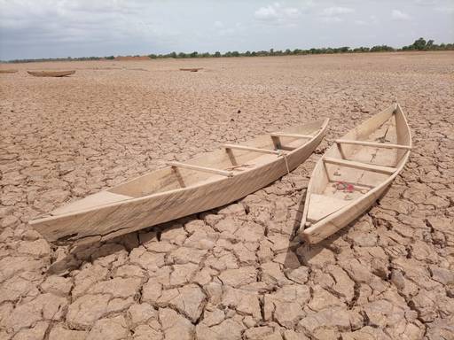 Foto von Holzbooten auf dem Grund eines ausgetrockneten Sees. Der Boden ist trocken und rissig.