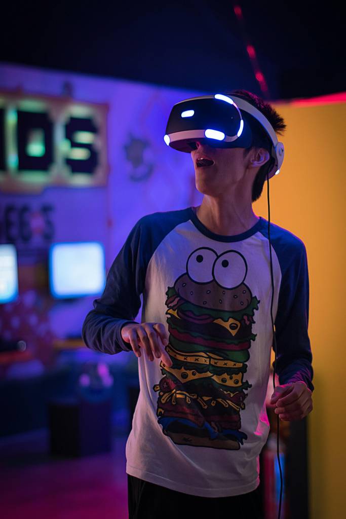 Vor einem dunklen und von Bildschirmen punktuell erleuchteten Hintergrund hat ein Junge hat eine VR-Brille aufgesetzt und staunt mit offenem Mund.