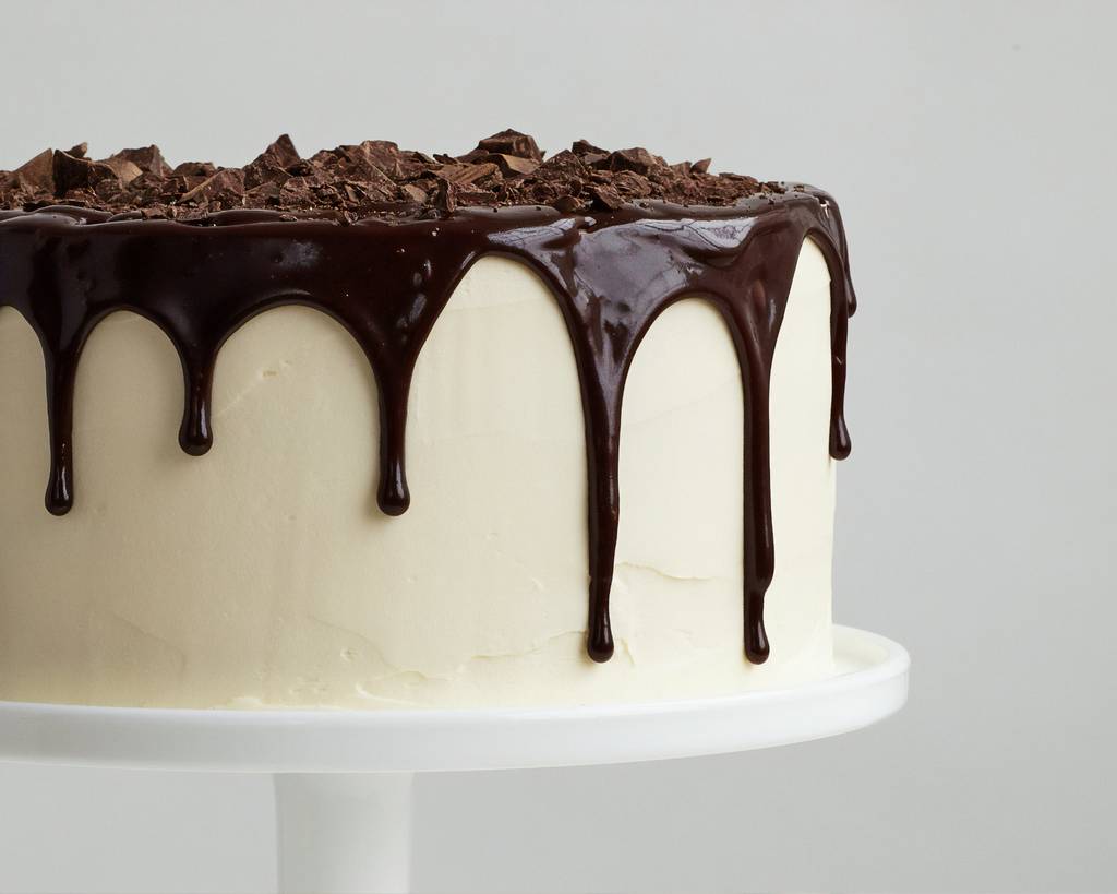 Ein weißer Kuchen auf einem Podest, überzogen mit einer dunklen Schokoglasur.